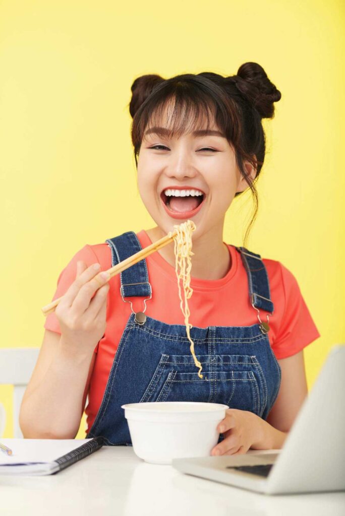 Chica asiática comiendo ramen de fideos con palillos chinos